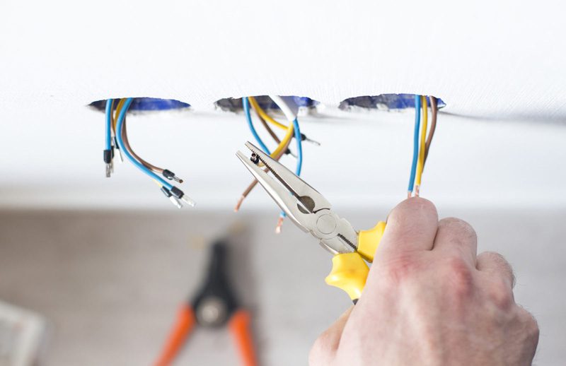 person using pliers on electrical wires hanging from ceiling